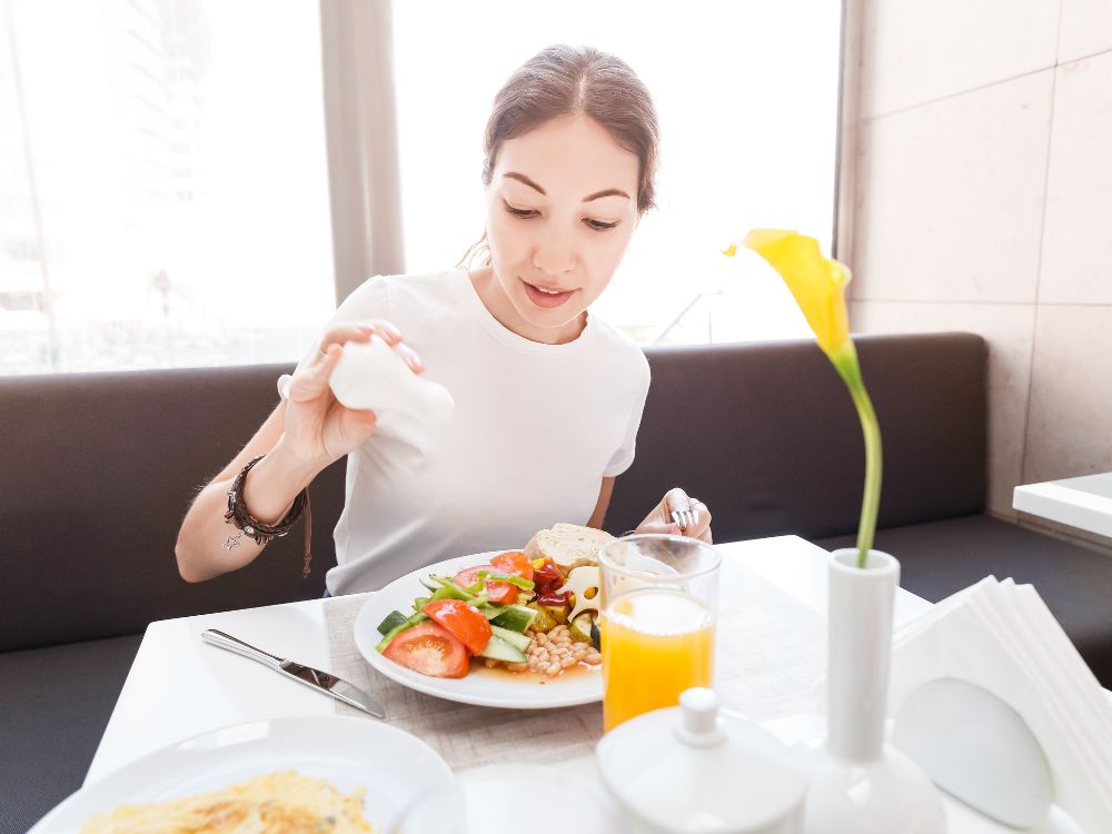 Mulher colocando salada no prato durante refeição saudável, ilustrando dicas de alimentação equilibrada com legumes, verduras e hábitos nutritivos no dia a dia.