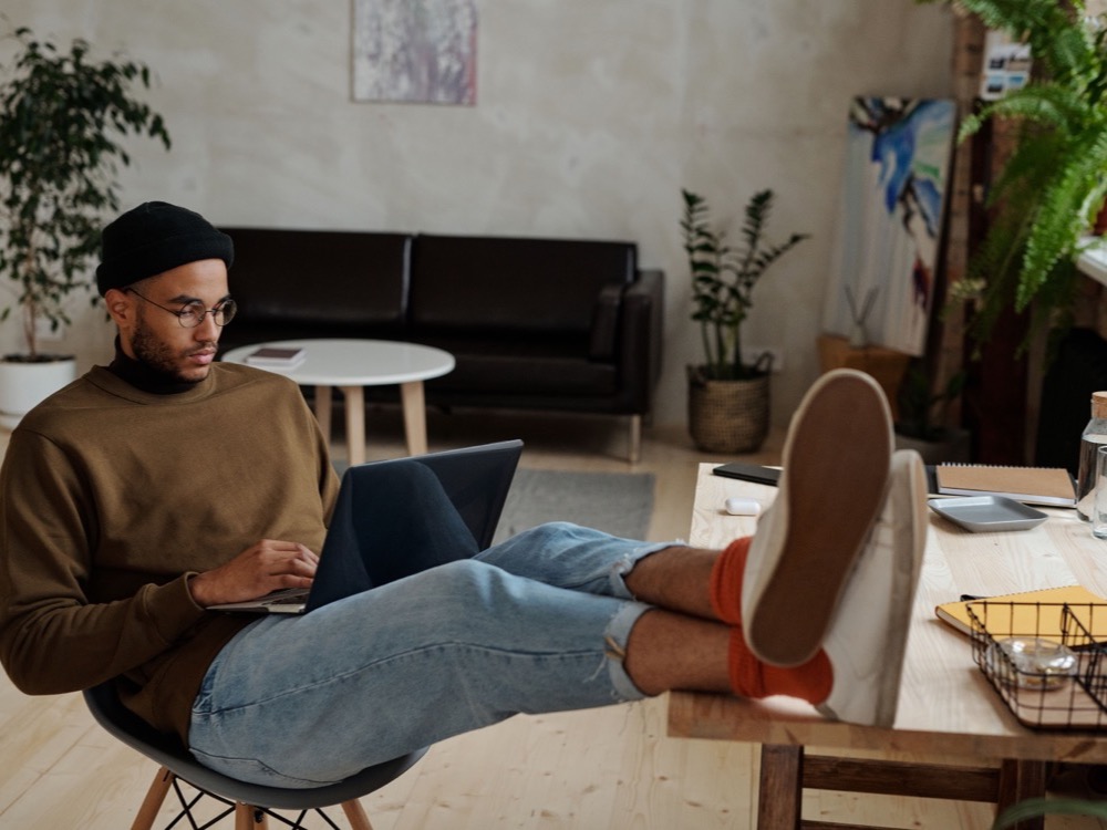 Profissional autônomo de home office, com um laptop no colo e com os pés em cima da mesa.