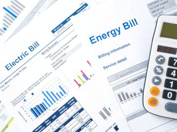 Contas de energia elétrica com gráficos de consumo e calculadora ao lado, ilustrando análise de gastos e eficiência no uso de energia no dia a dia.