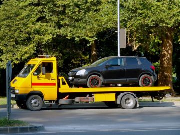 Caminhão guincho plataforma transportando carro preto em área urbana, ilustrando quanto custa um caminhão guincho no mercado.