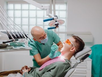 Dentista realizando atendimento odontológico em paciente na cadeira com uso de equipamentos clínicos no consultório.